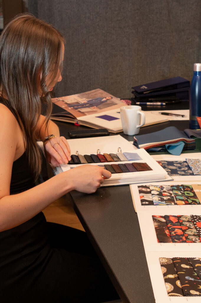 A woman sitting at a desk looking at books with different fabric swatches within